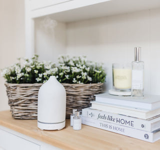 An electric diffuser with a couple of No. 1 White essential oils sitting on a wooden unit. There's also a No.1 White room spray and candle on top of some books.