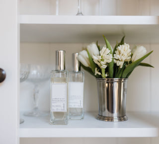 Two James & Co Fragrance No.1 White room sprays sit on a shelf next to a vase of white tulips and Lily Of The Valley.