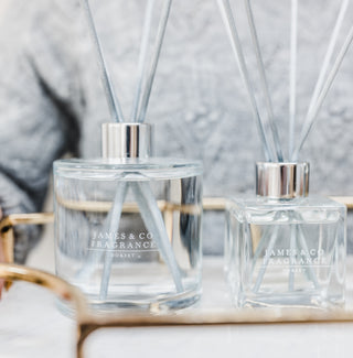 A set of two reed diffusers. One is larger and circle, the other is smaller and square. They both have grey reed diffuser sticks.