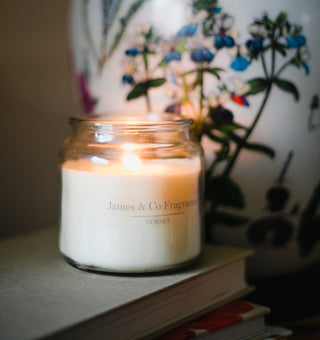 A lit candle in a glass jar next to a lamp
