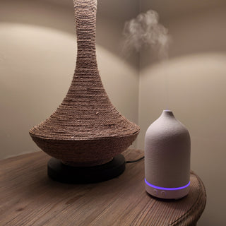 A white, ceramic diffuser, with a purple lit up band, sitting next to a lamp.