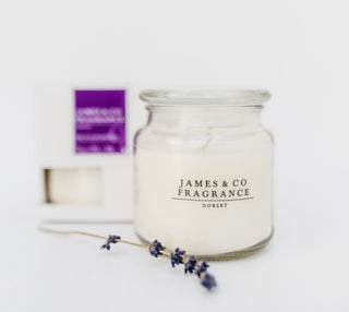 A glass jar lavender candle with a box sat behind.