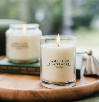 Our medium glass white candle, sitting on a wooden board, with our larger candle size blurred in the background.