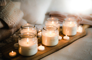 Several lit glass jar candles on a wooden board, with tealights scattered around them.