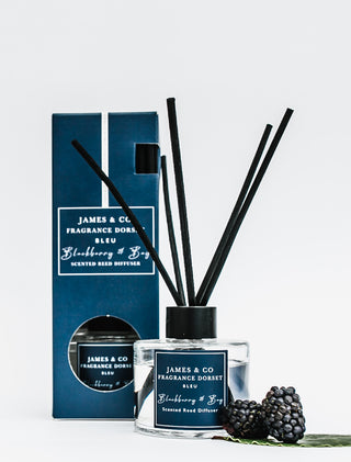 Vegan-friendly reed diffuser with packaging on a white background. A couple of blackberries and bay leaves next to the diffuser highlight the scent.