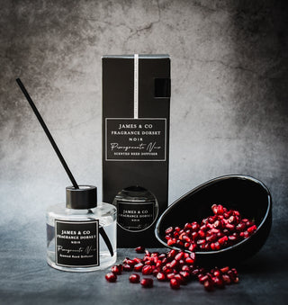 Pomegranate Noir Black 100ml Reed Diffuser sits with a bowl of pomegranate seeds