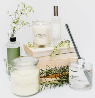 A white lit glass jar candle, sitting on a book next to a room spray and other various items.