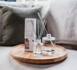 A boxed No.1 White diffuser, sat next to two open glass diffusers in different sizes. They are on a wooden board, on a soft service.