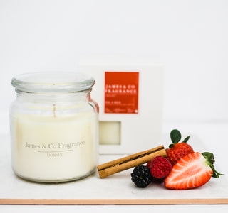 A white glass jar candle with a lid, sitting against a white background with a box. In front of it rests various berries and cinnamon sticks.