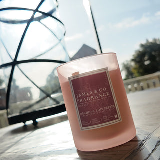 A pink pepper candle, in a frosted glass jar with a pink label, sitting in a sunny position on a kitchen table.