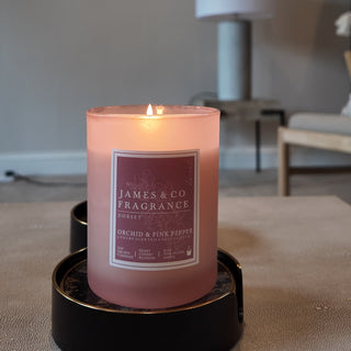 A lit pink pepper candle in a pink jar, with a frosted appearing sitting on a coffee table in a front room.