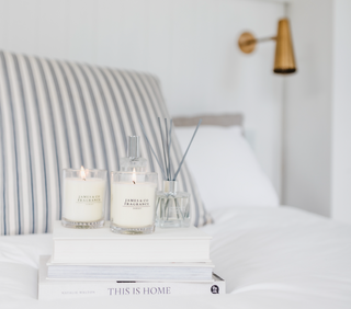 Two white jar candles which are lit, sitting on a pile of books in a bedroom space.