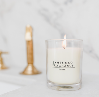 A white lit glass candle, sitting against a marble background in a bathroom.