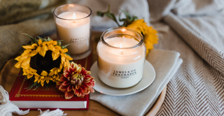 Two lit luxury candles, sat on a tray on a bed, with sunflowers scattered around