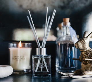 Fragrance diffuser, candle, and decorative items on a dark surface with a blurred background.