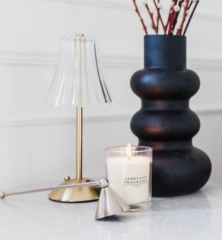 Candle with 'James & Co' branding next to a black vase and gold lamp on a white surface.