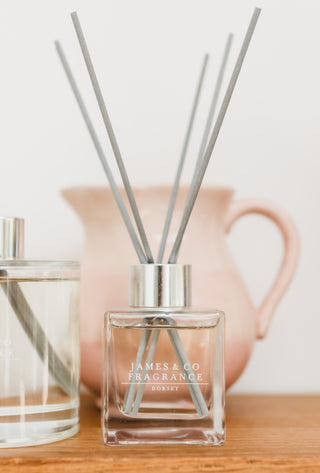 Diffuser bottle with sticks on a wooden surface with a pink ceramic item in the background