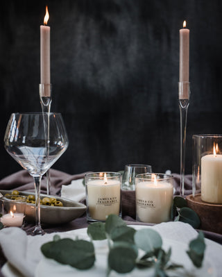 Candlelit table setting with wine glasses, candles, and greenery on a dark background