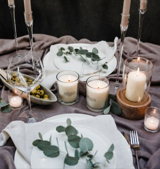 Table setting with candles, plates, and eucalyptus leaves on a dark background