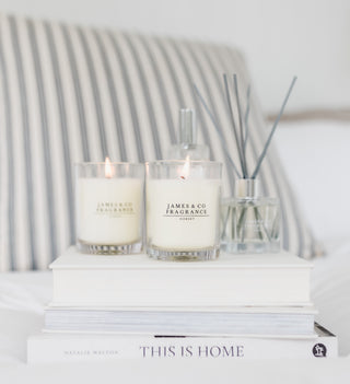 Two lit candles with 'James & Co Fragrance' branding on a stack of books with a blurred background.