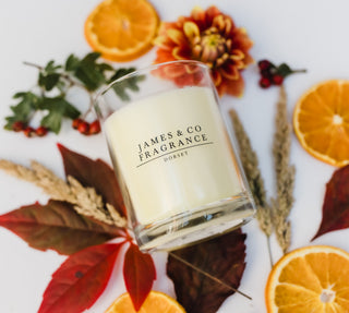 Candle with 'James & Co Fragrance Dorset' branding surrounded by autumn leaves and oranges.