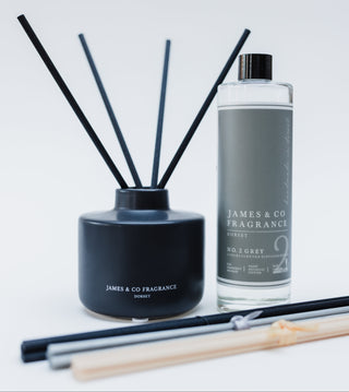 Black diffuser with reeds and a bottle of James & Co fragrance on a light gray background