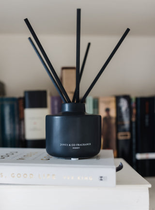 Black diffuser with sticks on a white surface with blurred books in the background