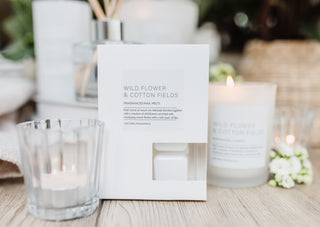 Candle packaging labeled 'Wild Flower & Cotton Fields' with candles and flowers in the background.