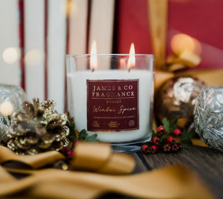 Winter spice glass candle, sat amongst gold and red decorations, ribbon, pinecones and berries.