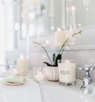 Candle with 'James & Co' branding on a bathroom counter with orchids and soap.