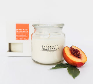 A white glass jar candle against a white background with a box in the background. In front of it sits a piece of apeicot.