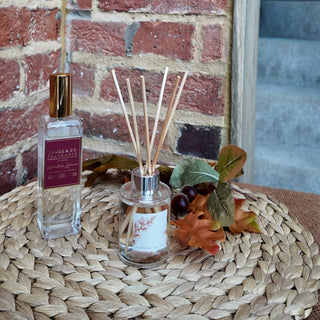 A room spray and reed diffuser, sitting on a side table with autumnal accessories. 