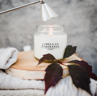 A white glass jar candle sitting on a wooden base. Above the candle is a snuffer about to be used. 