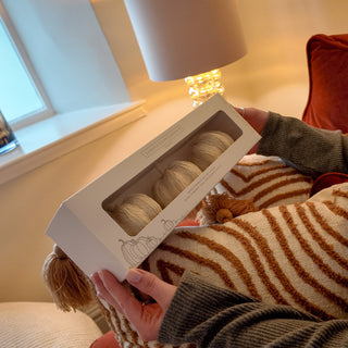 Person sitting on a striped chair holding a box of scented pumpkins in a cosy room.