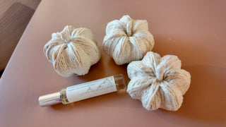 Three beige decorative pumpkins and a small bottle on a pink surface