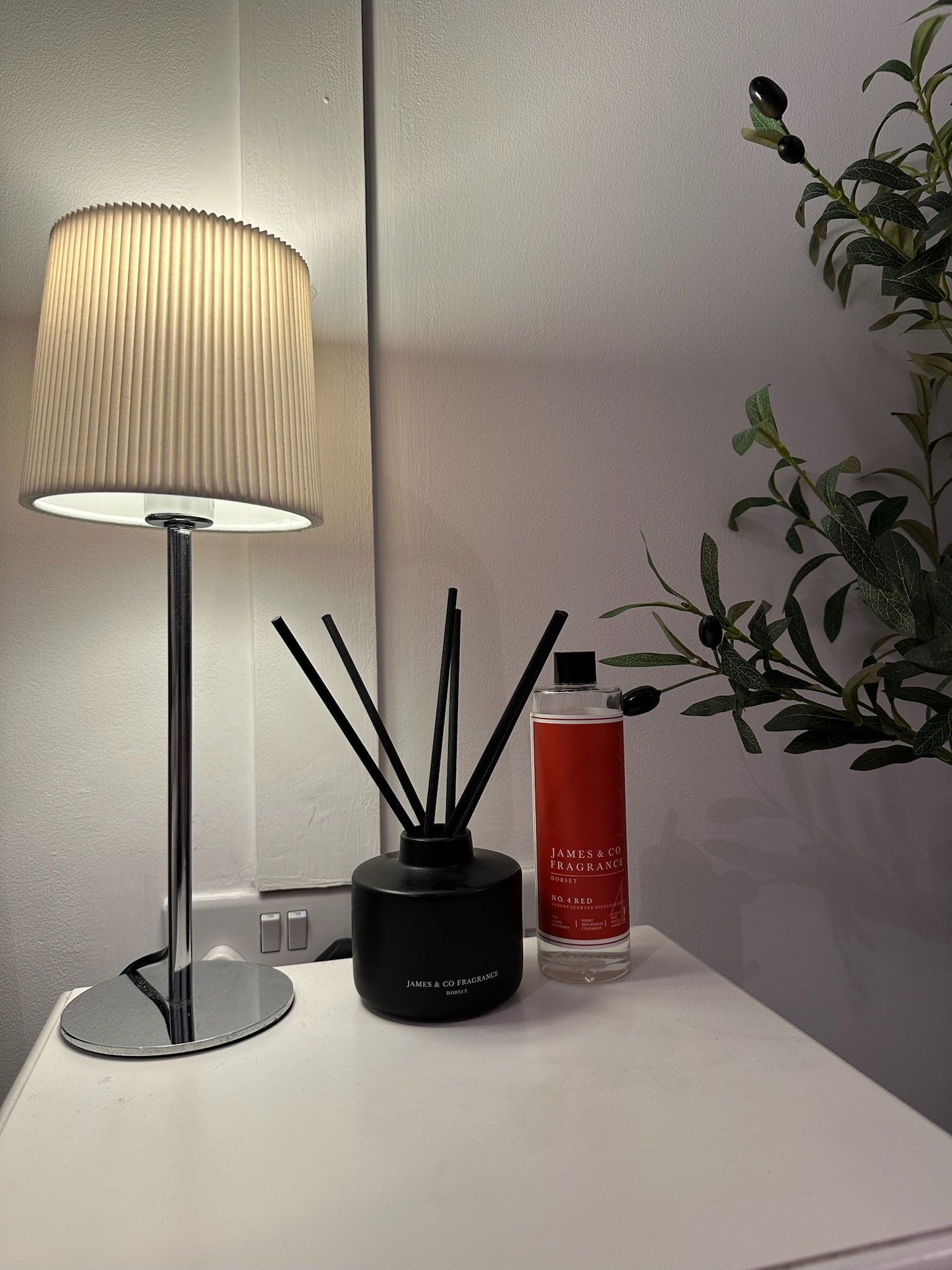 Table lamp, diffuser, and bottle on a surface with a plant in the background