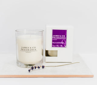 A glass jar candle with it's box sitting behind and a piece of lavender. 