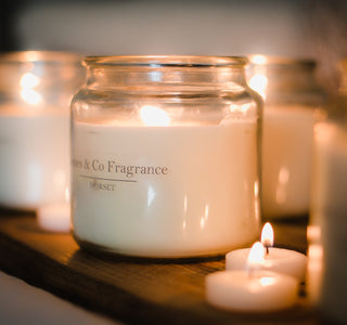 A lit glass jar candle sat on a shelf with various tealights and other candles in the background.