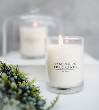Candle with 'James & Co Fragrance Dorset' label on a white surface with greenery.