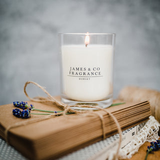 Lit candle with 'James & Co Fragrance Dorset' label on a wrapped gift with twine and flowers.