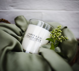 Candle with 'James & Co Fragrance' branding on a soft green fabric background