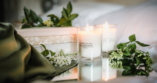 Two lit candles with 'James & Co' branding on a white surface with greenery.