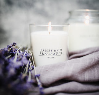 Candle with 'James & Co Fragrance Dorset' label surrounded by lavender flowers and fabric.