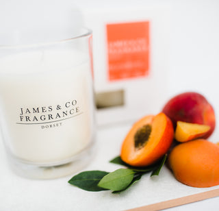 Candle labeled 'James & Co Fragrance Dorset' with peaches and leaves on a white surface