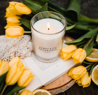 Candle with 'James & Co' branding surrounded by yellow tulips and lemons on a wooden surface.