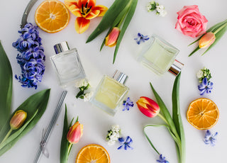 Three perfume bottles surrounded by flowers and fruits on a white background