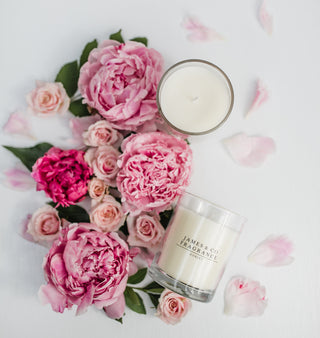Two candles from James Co Fragrances surrounded by pink flowers on a light background