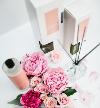 Floral arrangement with pink and red flowers, diffuser, and packaging on a white background