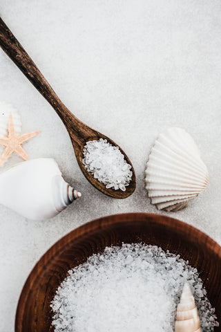 Wooden bowl and spoon filled with white salt, starfish, and seashells on a light background