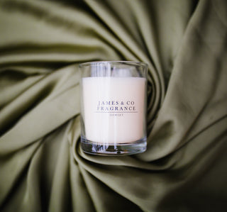 A medium glass jar candle laid on its back against a green background.